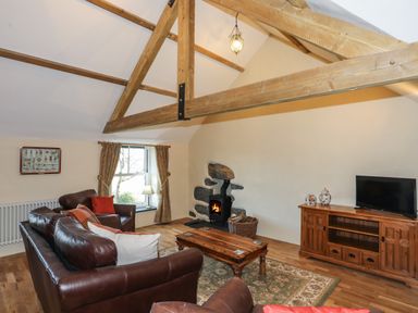 A living room with leather sofas a coffee table a wood stove and a wooden cabinet with a television at Bryn Moelyn Cottage in Yr Efail near Morfa Nefyn