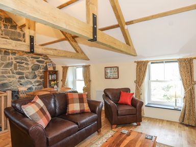 A living room with leather sofa and armchair near two windows with curtains at Bryn Moelyn Cottage in Yr Efail near Morfa Nefyn