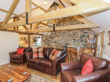 A living room with leather sofas wooden beams stone wall and a dining table at Bryn Moelyn Cottage in Yr Efail near Morfa Nefyn