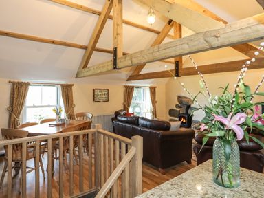 A living room with wooden beams a dining table with chairs and a wood burning stove at Bryn Moelyn Cottage in Yr Efail near Morfa Nefyn