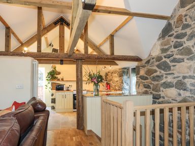 An open living area with brown leather sofas a kitchen with wooden beams and stone walls at Bryn Moelyn Cottage in Yr Efail near Morfa Nefyn