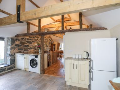 A kitchen area with washing machine dishwasher refrigerator and wooden beams at Bryn Moelyn Cottage in Yr Efail near Morfa Nefyn