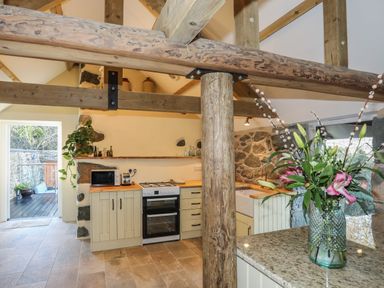 A kitchen with wooden beams and cabinets stone walls and a vase of flowers on a countertop at Bryn Moelyn Cottage in Yr Efail near Morfa Nefyn