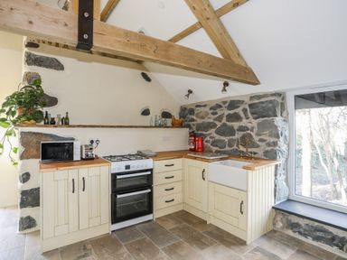 A kitchen with wooden beams stone walls a stove a microwave a toaster and a sink at Bryn Moelyn Cottage in Yr Efail near Morfa Nefyn