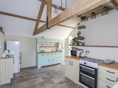A kitchen with wooden beams a stove a microwave and a blue cupboard with plates at Bryn Moelyn Cottage in Yr Efail near Morfa Nefyn