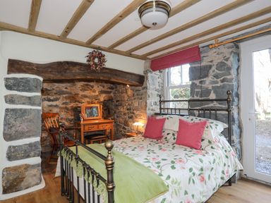 A bedroom with a metal bed, floral bedding, wooden chair, dressing table, stone walls and a window at Bryn Moelyn Cottage in Yr Efail near Morfa Nefyn