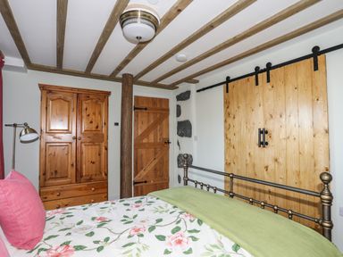 A bedroom with a wooden wardrobe wooden door exposed stone wall and a bed with floral bedding and green blanket at Bryn Moelyn Cottage in Yr Efail near Morfa Nefyn