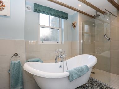A bathroom with a freestanding bathtub a glass shower enclosure towels on towel rings and a frosted window at Bryn Moelyn Cottage in Yr Efail near Morfa Nefyn