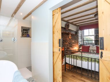 A bathroom with a shower and bathtub next to a bedroom with a metal bed frame and stone walls at Bryn Moelyn Cottage in Yr Efail near Morfa Nefyn