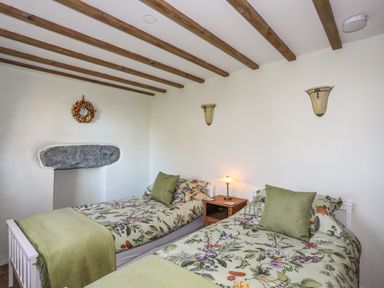 A bedroom with two single beds floral bedding and green pillows and blankets at Bryn Moelyn Cottage in Yr Efail near Morfa Nefyn