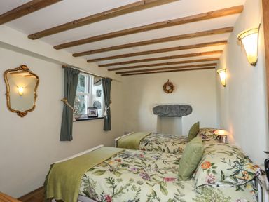 A bedroom with two single beds with floral bedding wooden ceiling beams and a window with curtains at Bryn Moelyn Cottage in Yr Efail near Morfa Nefyn
