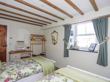 A bedroom with two single beds floral bedspreads a wooden dressing table a clothes rack a window with blue curtains and a mirror on the wall at Bryn Moelyn Cottage in Yr Efail near Morfa Nefyn