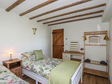 A bedroom with two single beds with floral bedding a wooden nightstand with a lamp a dressing table with a mirror and wooden door at Bryn Moelyn Cottage in Yr Efail near Morfa Nefyn