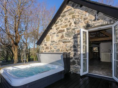 An outdoor hot tub next to an open door leading to a kitchen inside a stone cottage at Bryn Moelyn Cottage in Yr Efail near Morfa Nefyn