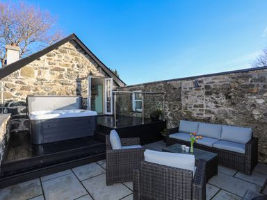 An outdoor patio with wicker furniture a hot tub and stone walls at Bryn Moelyn Cottage in Yr Efail near Morfa Nefyn