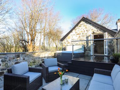 An outdoor patio with wicker seating and a glass table in front of a stone building at Bryn Moelyn Cottage in Yr Efail near Morfa Nefyn