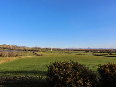 A landscape of green fields with bushes in the foreground a wind turbine and hills in the background at Bryn Moelyn Cottage in Yr Efail near Morfa Nefyn