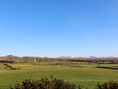 A landscape with green fields and a wind turbine with mountains in the background at Bryn Moelyn Cottage in Yr Efail near Morfa Nefyn