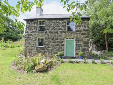 A stone cottage with a green door and flower beds in front at Bryn Moelyn Cottage in Yr Efail near Morfa Nefyn