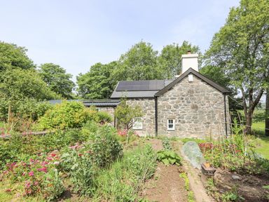 Stone house with solar panels on roof and garden with plants and flowers in front at Bryn Moelyn Cottage in Yr Efail near Morfa Nefyn