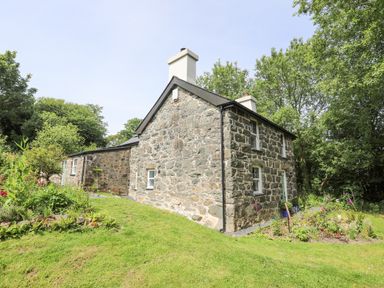 A stone cottage with chimneys surrounded by grass and trees at Bryn Moelyn Cottage in Yr Efail near Morfa Nefyn