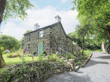 A stone cottage with a green door surrounded by trees and a gravel pathway at Bryn Moelyn Cottage in Yr Efail near Morfa Nefyn