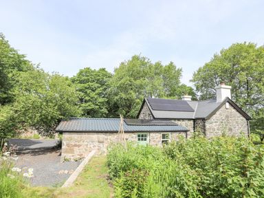 A stone cottage with solar panels on the roof surrounded by trees and plants at Bryn Moelyn Cottage in Yr Efail near Morfa Nefyn