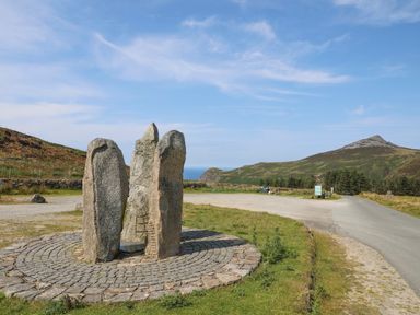 A stone circle sculpture near a road with hills and a clear sky in the background at Bryn Moelyn Cottage in Yr Efail near Morfa Nefyn