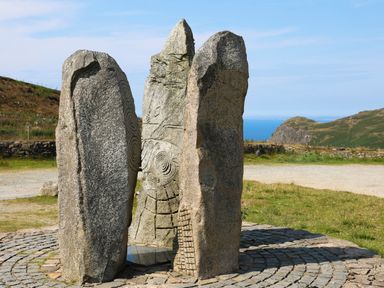 Three tall carved standing stones arranged in a circle on a stone paved area with hills and sea in the background at Bryn Moelyn Cottage in Yr Efail near Morfa Nefyn