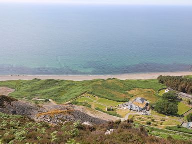A coastal landscape with green hills a sandy beach and buildings near the shoreline at Bryn Moelyn Cottage in Yr Efail near Morfa Nefyn