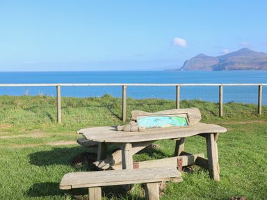 A weathered wooden bench and table on grass near a fence with sea and hills in the background at Bryn Moelyn Cottage in Yr Efail near Morfa Nefyn