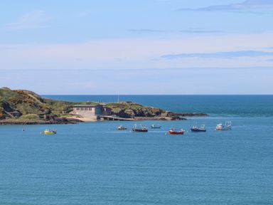 Boats anchored in a bay near a rocky shoreline with a building on the coast at Bryn Moelyn Cottage in Yr Efail near Morfa Nefyn