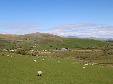 A rural landscape with green fields, grazing sheep, hills in the background, and scattered houses at Bryn Moelyn Cottage in Yr Efail near Morfa Nefyn