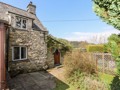A stone exterior cottage with two windows and a wooden door near a garden and lattice fence at Gilfachwydd in Islawrdref near Dolgellau