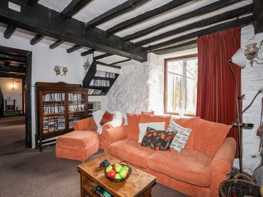 A living room with orange sofas a wooden coffee table a bookshelf and a window with red curtains at Gilfachwydd in Islawrdref near Dolgellau