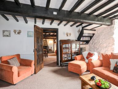 A sitting room with orange armchairs and sofa wooden cabinet and exposed wooden ceiling beams at Gilfachwydd Islawrdref near Dolgellau