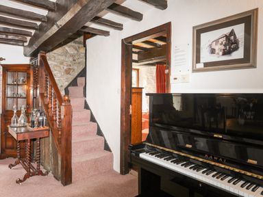 A room with a staircase a black piano a wooden cabinet and a table with glassware at Gilfachwydd in Islawrdref near Dolgellau