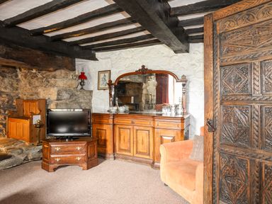 A room with wooden furniture including a TV stand, dresser with a mirror, an armchair, and stone wall at Gilfachwydd in Islawrdref near Dolgellau