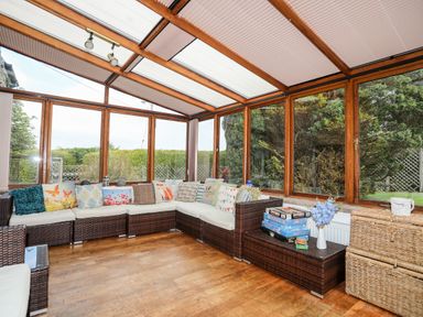 A sunroom with wicker sectional sofa and board games on a table at Gilfachwydd in Islawrdref near Dolgellau