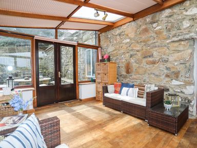 A sunroom with wicker furniture cushions wooden floor and stone wall at Gilfachwydd in Islawrdref near Dolgellau
