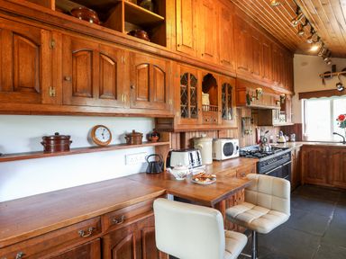 A kitchen with wooden cabinets stools a stove and appliances at Gilfachwydd in Islawrdref near Dolgellau