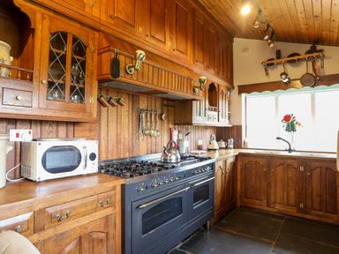 A kitchen with wooden cabinets a black oven a microwave and a window with flowers at Gilfachwydd in Islawrdref near Dolgellau