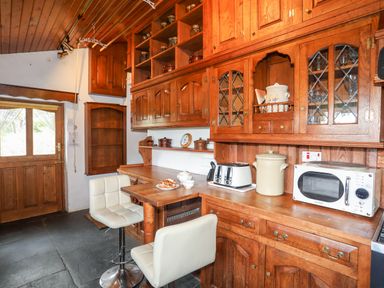 A kitchen with wooden cabinets two white chairs a microwave and a toaster at Gilfachwydd Islawrdref near Dolgellau