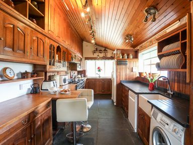 A kitchen with wooden cabinets black countertops appliances and a white chair at Gilfachwydd Islawrdref near Dolgellau