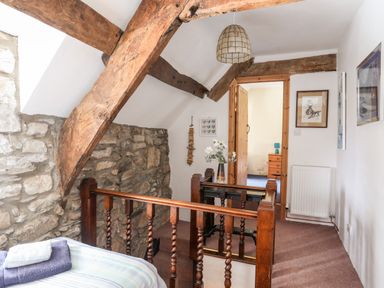 A hallway with wooden beams stone wall and a bed with towels at Gilfachwydd Islawrdref near Dolgellau