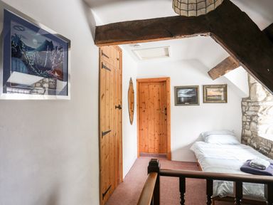 A small bedroom with a single bed next to a stone wall wooden doors and framed pictures on the wall at Gilfachwydd Islawrdref near Dolgellau
