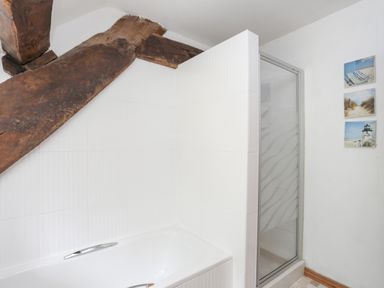 A bathroom with a white bathtub wooden beam above and a glass shower enclosure with beach-themed wall art at Gilfachwydd Islawrdref near Dolgellau