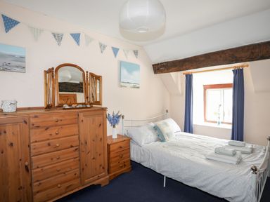 A bedroom with a double bed beside a window and a wooden dresser with a mirror and a small bedside table at Gilfachwydd Islawrdref near Dolgellau