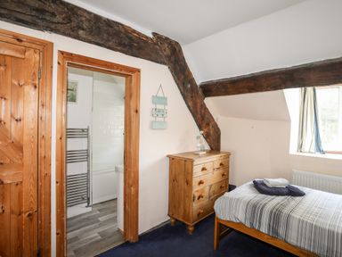 A bedroom with a wooden chest of drawers a bed with striped bedding and an open door to a bathroom at Gilfachwydd Islawrdref near Dolgellau