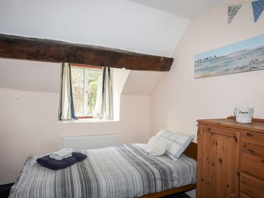 A bedroom with a single bed under a window with curtains and a wooden cabinet at Gilfachwydd Islawrdref near Dolgellau